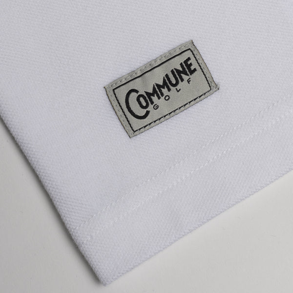 Détail du t-shirt blanc Commune golf : étiquette tissée et piqué de coton bio. T-shirt confectionné au Portugal dans un atelier certifié GOTS